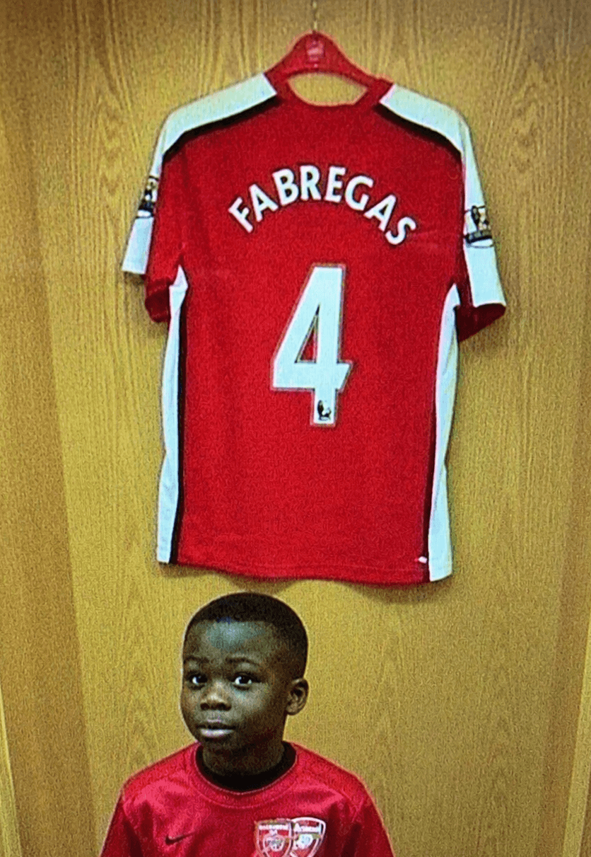 young boy sitting in locker room in front of soccer jersey
