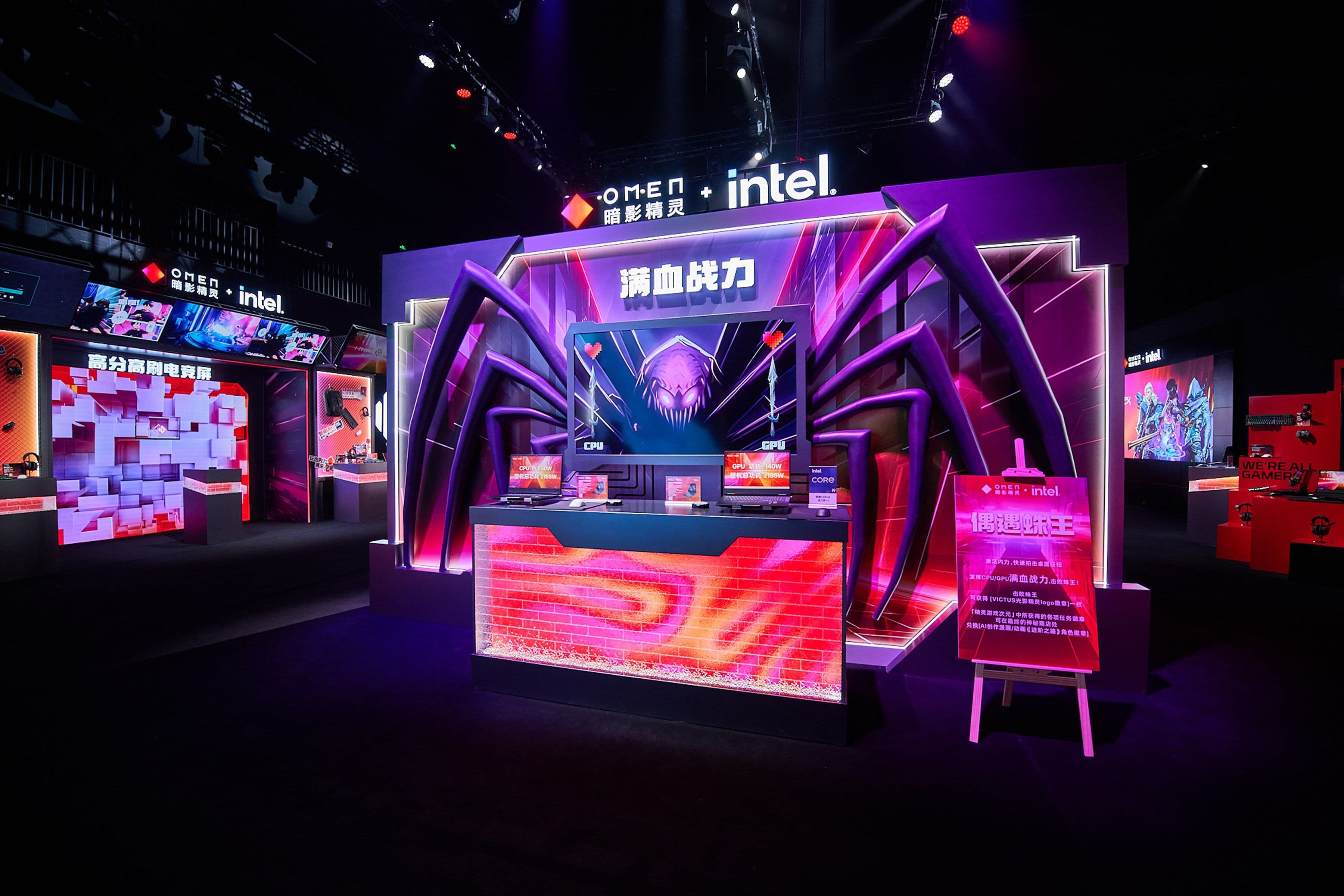 Vibrant gaming booth with neon lights, spider design, and Intel branding. Displays feature laptops and promotional materials.