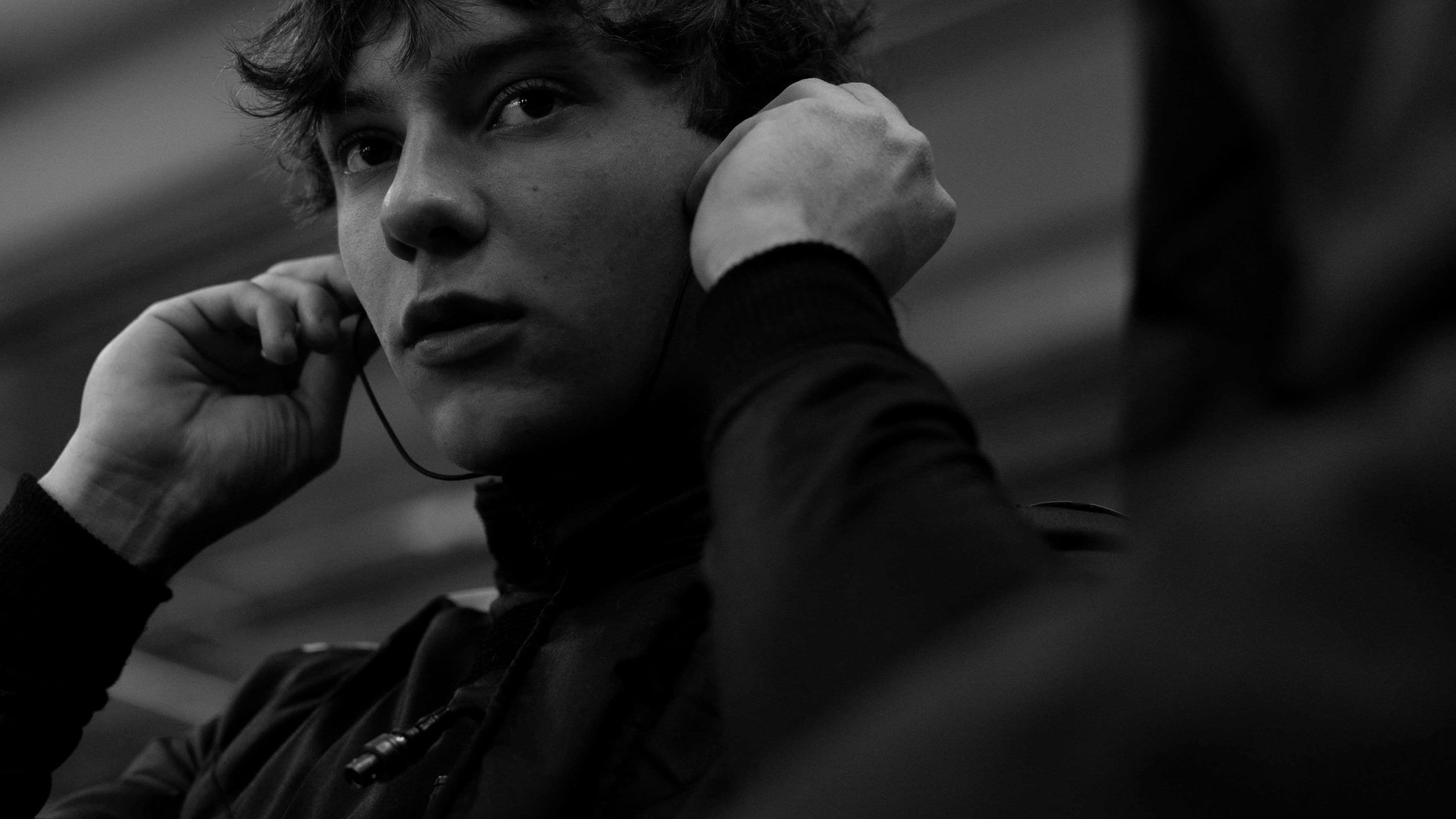 Person adjusting earphones, looking thoughtful, in black and white.
