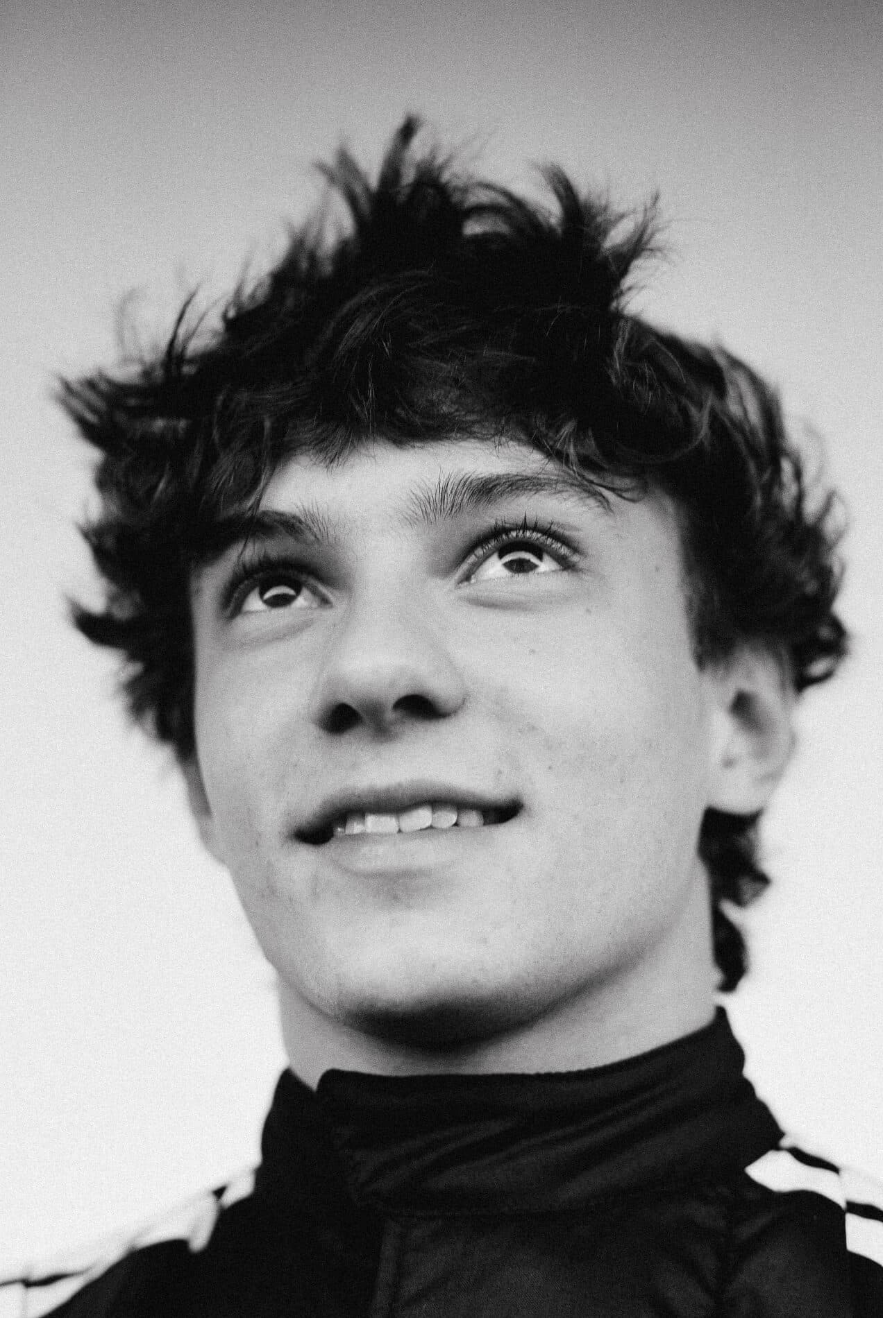 Young person with curly hair, looking upwards, wearing a jacket. Black and white photo.