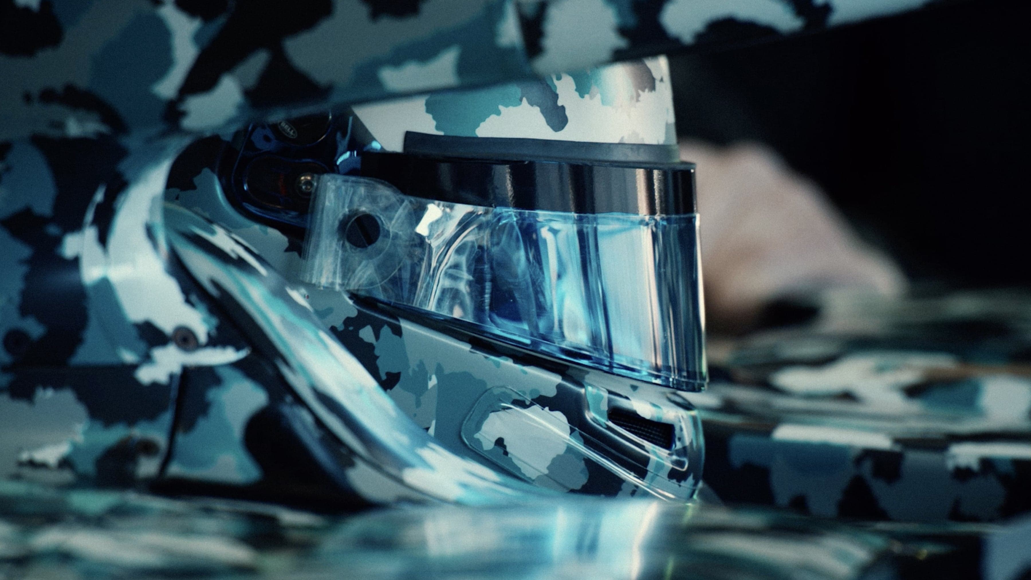 Close-up of a futuristic F1 helmet with a blue-tinted visor, featuring a blue and white camouflage pattern.