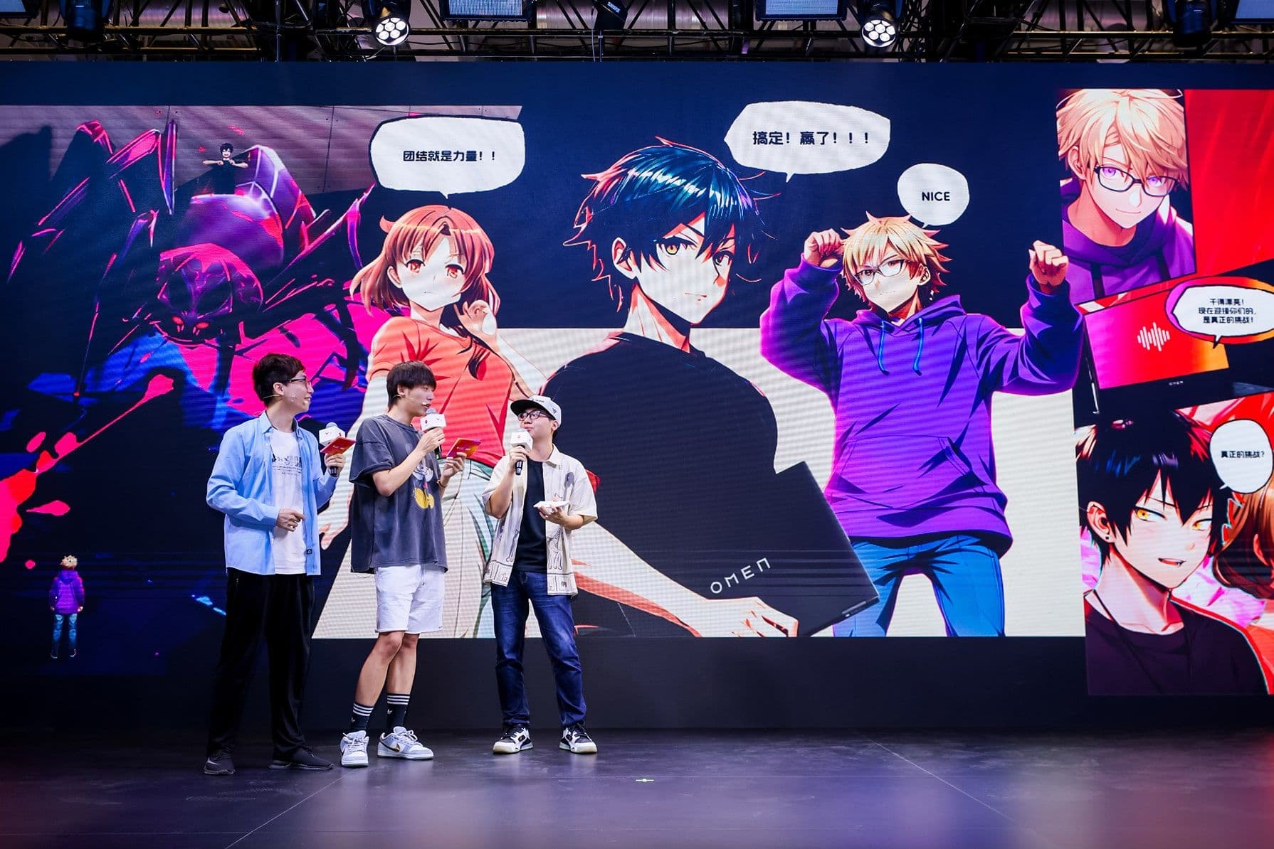 Three people on stage with microphones in front of a large anime-themed screen displaying colorful characters and speech bubbles.