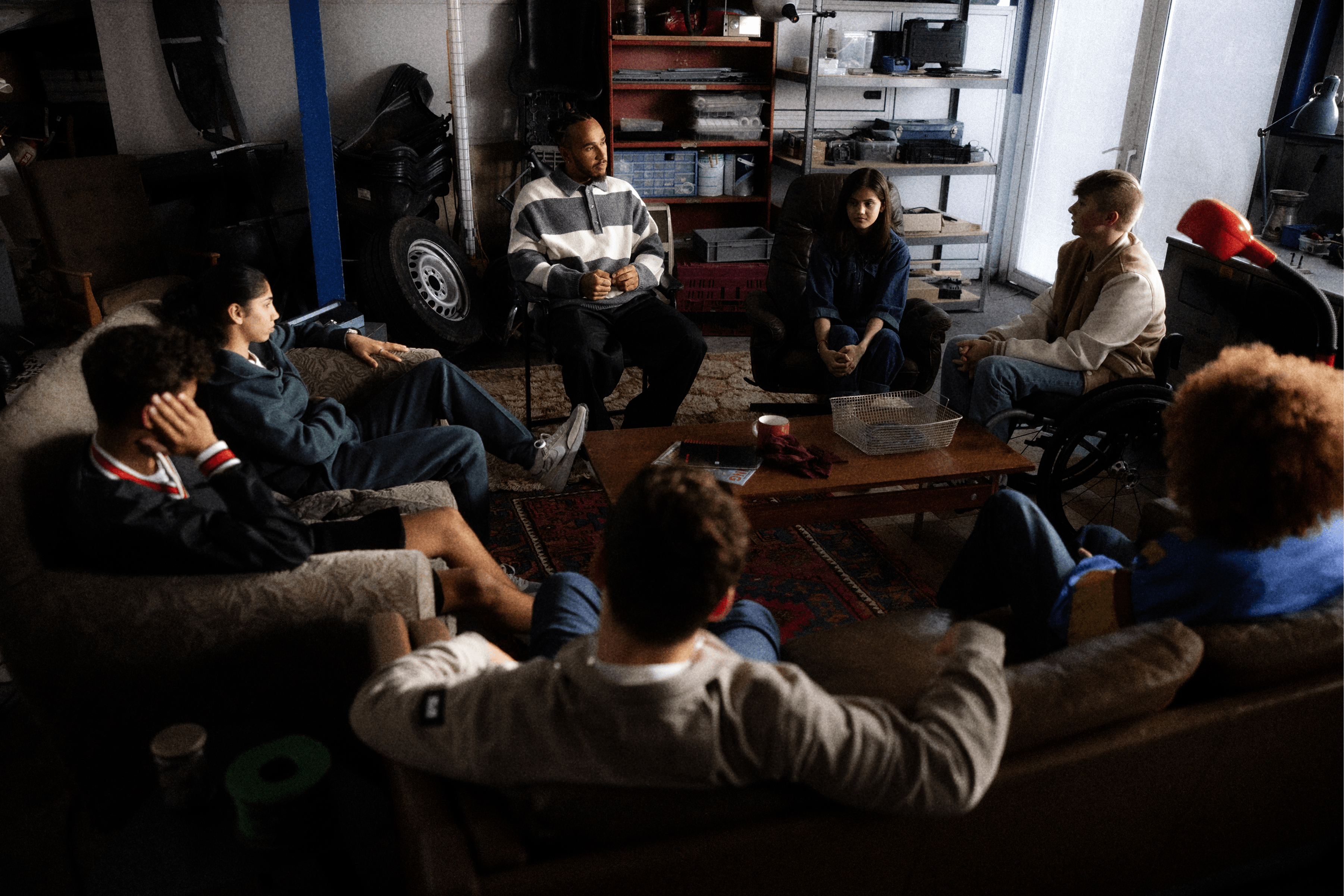 Seven people sitting in a circle on couches in a garage setting.